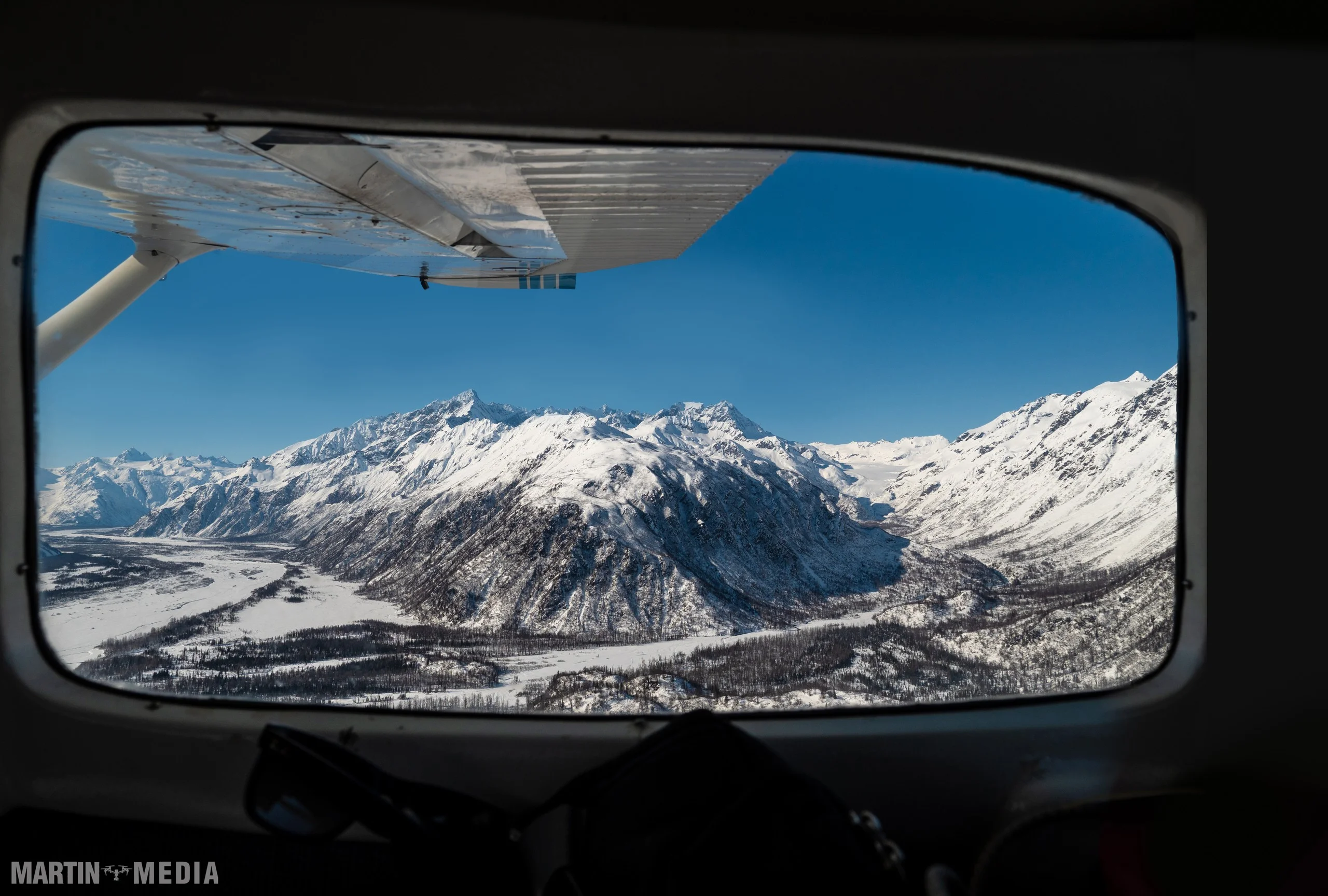 Aerial view from bush plane wing overlooking snowcapped Alaskan mountain ridges