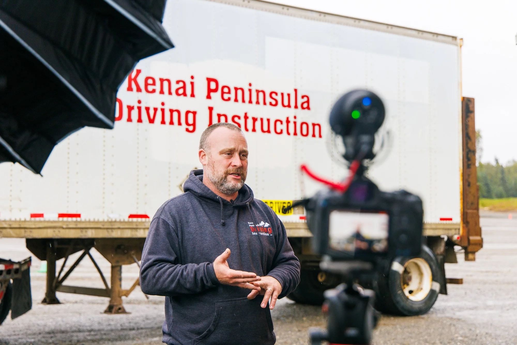 Owner and instructor of Kenai Peninsula Driving Instruction talking to camera in front of commercial semi truck trailer