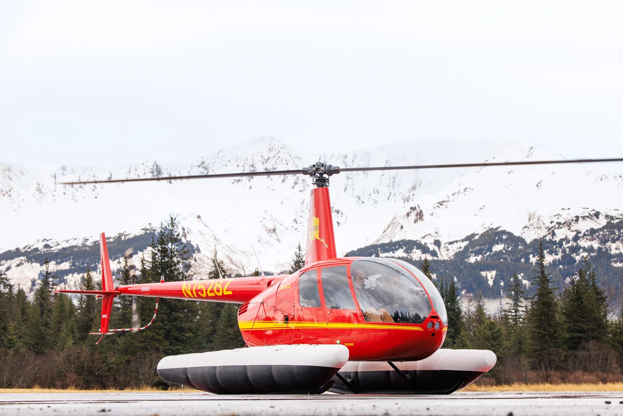 Red Robinson helicopter on floats with snowcapped Alaskan mountains in Seward