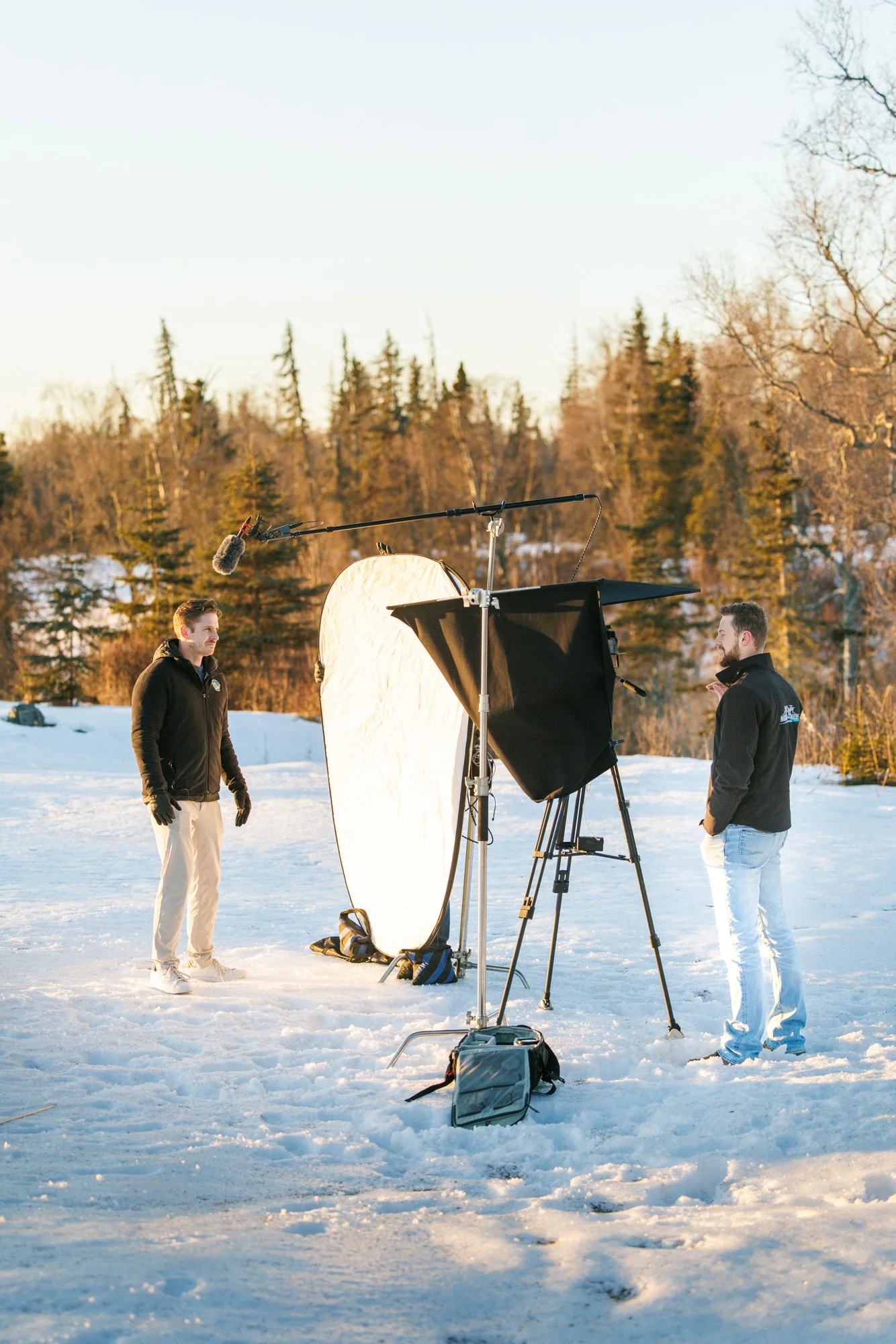 Martin Media production crew filming commercial presenter in sub-zero snow field with softbox and boom mic during Alaskan golden hour
